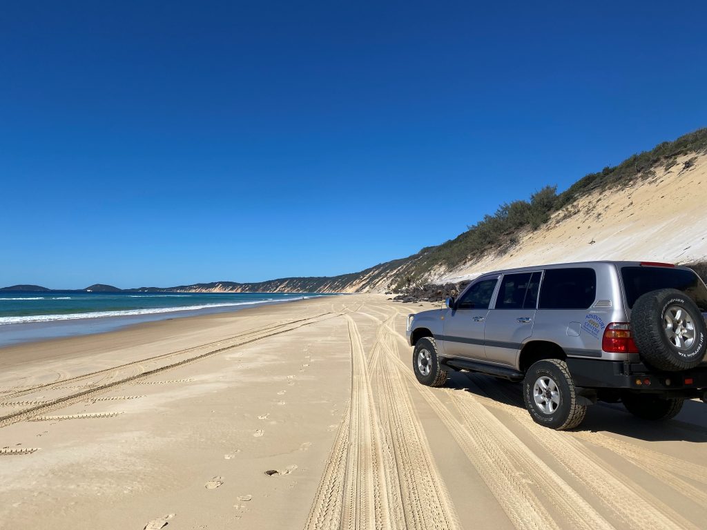 Rainbow Beach Adventure Centre 4wd 'Benny' parked on Rainbow Beach looking towards the coloured sands and Double Island Point.