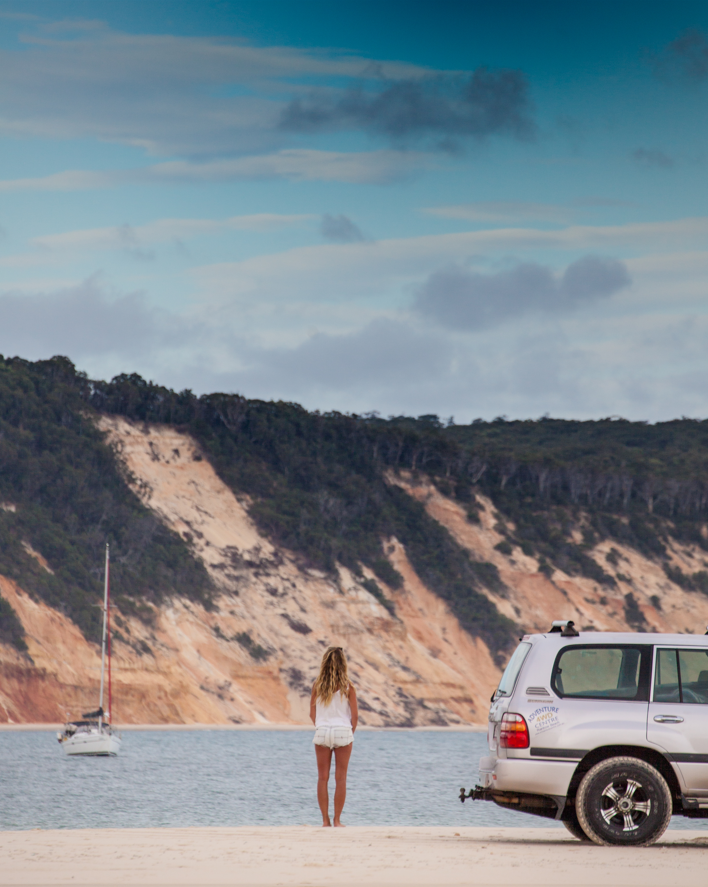 Rainbow Beach Adventure Centre self-drive 4wd parked at Double Island Point, looking back towards the coloured sands, across the lagoon with a yacht moored.